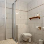 Badezimmer mit Dusche, Toilette und Waschbecken. Weiße Fliesen und Holzregal.