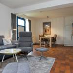 Wohnzimmer mit Sofa, Sessel und Esstisch. Küche im Hintergrund. Terrakottaboden.