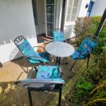 Terrasse mit runder Tisch und vier Stühlen mit blau-tropischen Kissen.