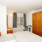 Schlafzimmer mit Bett, Holzschrank, Nachttisch und Fenster mit Vorhängen.
