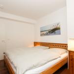 Schlafzimmer mit Holzbett, Kleiderschrank und Nachttisch mit Lampe.
