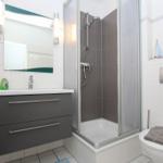 Badezimmer mit Dusche, Waschbecken und Toilette. Fliesenwand und Spiegel.