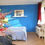 Schlafzimmer mit blauer Wand, Bett, Schreibtisch und Blumenarrangement.