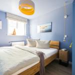 Schlafzimmer mit blauen Wänden, Holzbett und Fenster mit Segelboot.
