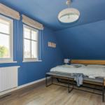 Schlafzimmer mit blauen Wänden, Holzboden und Bett mit Holzkopfteil.