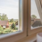 Durch das Fenster blickt man auf ein Dorf mit Strohdächern und Grünflächen.