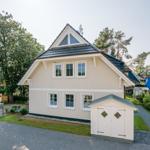 Ein zweistöckiges Haus mit weißem Anstrich und grauem Dach. Vor dem Haus steht ein kleiner weißer Schuppen.