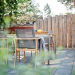 Terrasse mit Tisch und Stühlen, Holzgeländer und Bäumen im Hintergrund.
