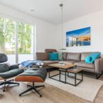Wohnzimmer mit braunem Sofa, Ecksessel und Holzboden. Große Fenster und Wandbild.