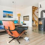 Wohnzimmer mit Holzboden, Sofa, Stuhl und Kaminofen. Treppenhaus und Wandbild sind sichtbar.