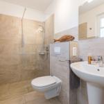 Badezimmer mit Dusche, Toilette und Waschbecken. Wandfliesen und Spiegel sichtbar.