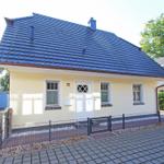 Ein kleines Haus mit gelber Fassade und dunkelblauem Dach, umgeben von Grünflächen und einem Zaun.