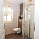 Badezimmer mit Dusche, Toilette und Fenster. Fliesenwand und Boden.