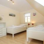 Zimmer mit zwei Betten, Schrank und Fenster unter Dachschräge.