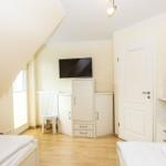 Zimmer mit zwei Betten, TV, Schrank und Pflanze. Dachschräge und Fenster.