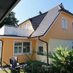 Ein gelbes Haus mit Balkon und Dachgaube. Im Vordergrund sind Grünflächen und ein Fahrrad sichtbar.