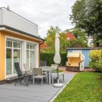 Terrasse mit Tisch, Stühlen und Sonnenschirm neben gelbem Haus mit Garten.