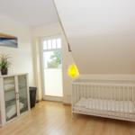 Kinderzimmer mit weißem Kinderbett, Schrank, Pflanze und Fenster.