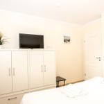 Schlafzimmer mit weißem Schrank, Fernseher und Bett mit Handtüchern.