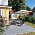 Terrasse mit Tisch, Stühlen und Sonnenschirm. Hintergrund: Garten, Bäume und Nachbarhäuser.
