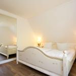 Schlafzimmer mit weißem Bett, Nachttisch und Spiegel an der Wand.