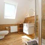 Badezimmer mit Dusche, Waschbecken und Toilette. Holzoptik und Dachfenster.