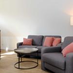 Ein Wohnzimmer mit grauem Sofa, rosa Kissen, Tisch und Stehlampe.