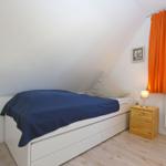 Ein Schlafzimmer mit Dachschrägen, Bett, Nachttisch und Fenster mit orangefarbenen Vorhängen.