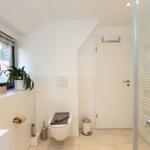 Badezimmer mit Toilette, Fenster, Pflanze und Dusche.