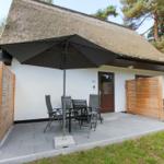 Haus mit Strohdach, Terrasse mit Tisch, Stühlen und Sonnenschirm.