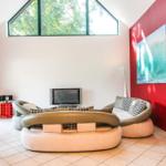 Wohnzimmer mit runden Sofas, roten Wänden und großem Fenster. Wandbild zeigt Wellen.