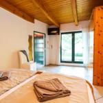 Schlafzimmer mit Bett, Holzbalkendecke und Fenster. Holzwand und TV sichtbar.