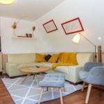 Wohnzimmer mit Sofa, Stuhl und Tisch. Wand mit Bildern und Regal.