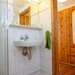 Badezimmer mit Dusche, Waschbecken und Holzschrank.