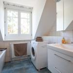 Badezimmer mit Waschmaschine, Badewanne und Waschtisch unter Dachschrägen.