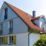 Haus mit blau-weißem Streifenfassade, rotem Dach und grünen Fensterläden.