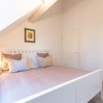 Schlafzimmer mit weißem Bett, Nachttisch und Kleiderschrank unter Dachschrägen.
