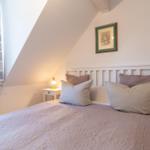 Schlafzimmer mit Bett, Nachttisch und Fenster unter Dachschrägen.