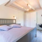 Schlafzimmer mit Bett, Schrank und Schreibtisch unter Holzbalkendecke.