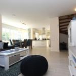 Wohnzimmer mit Sofa, Couchtisch und Fernseher. Küche und Essbereich im Hintergrund.