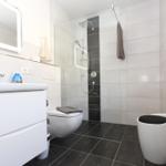 Badezimmer mit Dusche, Waschbecken und Toilette. Fliesenboden und Spiegel.