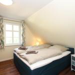 Schlafzimmer mit Doppelbett, Fenster und Nachttisch.