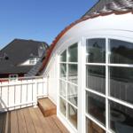 Terrasse mit Holzboden und weißer Brüstung. Blick auf ein Haus mit Satellitenschüssel.
