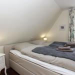 Schlafzimmer mit Doppelbett, Nachttisch und Fenster mit Vorhängen.