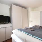 Schlafzimmer mit Bett, Kleiderschrank und Fernseher. Tür führt in angrenzenden Raum.