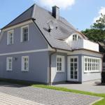 Ein graues Haus mit weißen Fenstern und einem Balkon. Außenterrasse mit Tisch und Stühlen.