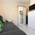 Grauer Sofa mit grün-weißen Kissen, weißer Schrank und Fernseher auf Holzkonsole.