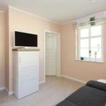 Wohnzimmer mit Sofa, TV und Fenster. Wandfarbe rosa, Holzboden.