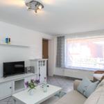 Wohnzimmer mit Sofa, Fernseher und Tisch. Fenster mit Blick auf Balkon.