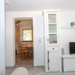 Wohnzimmer mit TV und weißen Schränken. Durchgang zur Küche mit Tisch und Stühlen.